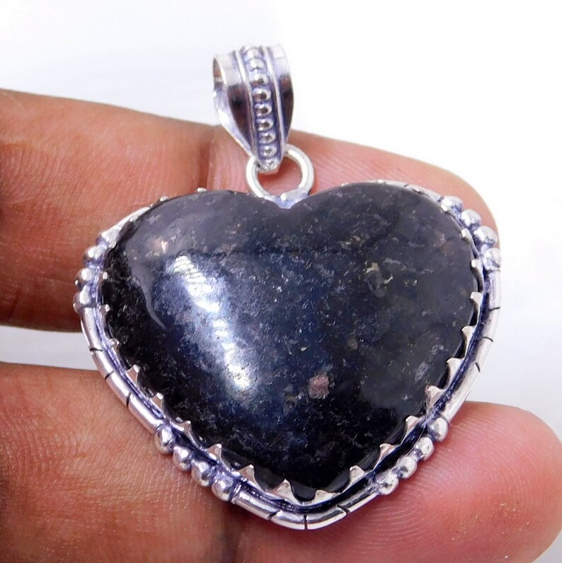 Pu&ograve; includere: Un ciondolo a forma di cuore in argento con una pietra preziosa nera. Il ciondolo ha un bordo in argento dettagliato con piccole perle.