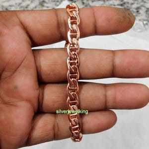Peut inclure: Un bracelet à chaîne de couleur or rose composé d'une série de maillons ovales entrelacés, chacun présentant un motif de surface texturé et rainuré. Le métal a une finition polie et réfléchissante. Le texte silverjewelking est visible.
