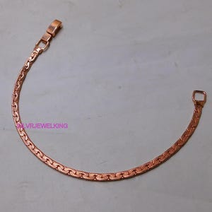 Peut inclure: Un bracelet de couleur cuivrée avec un design plat en forme de chaîne. Le bracelet est doté d'un fermoir rectangulaire et d'un motif texturé sur toute sa longueur. Le texte "SLVRJEWELKING" est visible sur le bracelet.