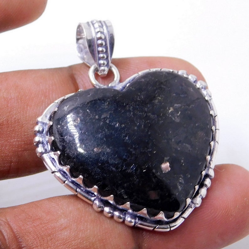 Pu&ograve; includere: Un ciondolo a forma di cuore in argento con una pietra preziosa nera. Il ciondolo ha un bordo in argento dettagliato con piccole perle.