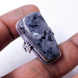 May include: A silver ring featuring a large, rectangular, grey and black gemstone. The gemstone has a speckled pattern.