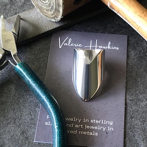 May include: A silver ring with a pointed, V-shaped design. The ring is displayed on a card with the text "Valerie Hawkins Jewelry in sterling and art jewelry in mixed metals".
