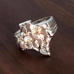 May include: A silver ring with a textured, abstract design. The ring has a wide band and a pointed top.