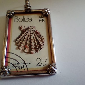 May include: A rectangular pendant featuring a vintage Belize stamp with a seashell illustration. The stamp is set in a silver-toned frame with decorative accents. The text "Belize" and "25¢" are visible.