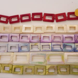 May include: Rows of square belt buckles in various colors. The top row is red, followed by cream, lavender, iridescent blue, and olive green. Each buckle has a rectangular opening in the center.