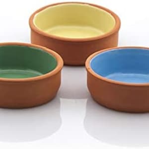 May include: Three small, round terracotta bowls with colourful interiors. One bowl has a green interior, another has a yellow interior, and the third has a blue interior. The bowls are arranged on a white surface.