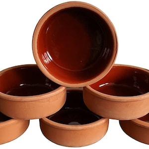 May include: A collection of six small, round bowls in terracotta. The bowls have a dark brown interior and a lighter, unglazed exterior. They are arranged to display their shape and colour.