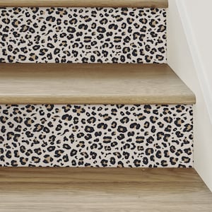 Puede incluir: Primer plano de una escalera de madera con un patrón de estampado de leopardo en los bordes de cada escalón. La escalera está pintada de un color marrón claro y el patrón es en negro, marrón y blanco.