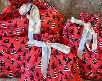 May include: Four red Christmas gift bags with a repeating pattern of black and white Christmas trees. Each bag is tied with a silver ribbon. The bags are different sizes and are gathered at the top.