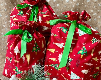 May include: Three red Christmas gift bags with green ribbon ties. The bags are patterned with white and yellow Christmas trees and snowflakes. The bags are of varying sizes and are gathered at the top.