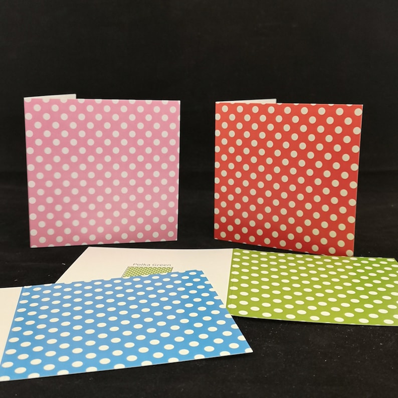 May include: Four square cards with white polka dots on different colored backgrounds. The colors are pink, red, blue, and green.