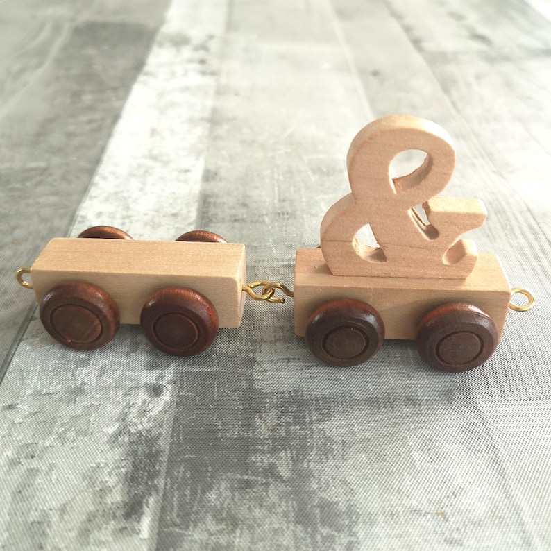 May include: Wooden toy train with a brown ampersand symbol on the front car. The train has brown wheels and is made of natural wood.