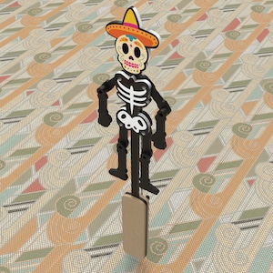 Pode incluir: Um esqueleto preto vestindo um sombrero colorido com um rosto de caveira e desenhos florais. O esqueleto está em pé em um bastão de madeira.