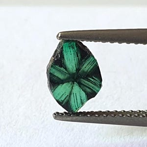 May include: A green emerald gemstone with a star-shaped pattern, held by tweezers.