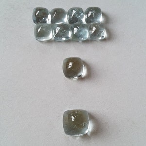 Pode incluir: Dez pedras preciosas quadradas de cor azul claro dispostas em duas filas, com duas pedras preciosas adicionais abaixo.