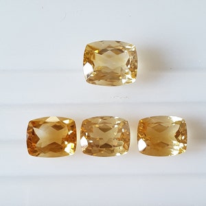 May include: Four golden yellow cushion-cut gemstones on a white background.