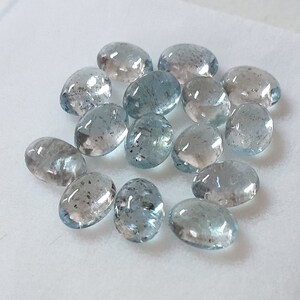 May include: A collection of oval-shaped aquamarine gemstones, ranging in size and shade of blue. The stones are smooth and polished, with a translucent appearance.