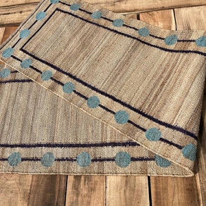 Puede incluir: Una alfombra tejida con un borde azul y negro. El borde tiene un patrón repetido de círculos.