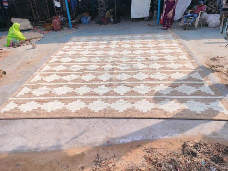 May include: A large, rectangular, woven rug with a geometric pattern. The rug is made of natural fibres and has a light brown and white colour scheme.
