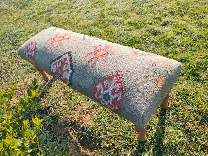 Op de afbeelding: Een grijze en witte gepatroneerde bank met houten poten. De bank heeft een traditioneel tapijtontwerp met rode, blauwe en gele accenten.