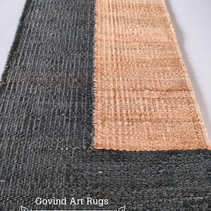 May include: A handwoven rug with a geometric design. The rug is made of natural fibers and has a dark blue and light brown color scheme. The rug is labeled "Govind Art Rugs".