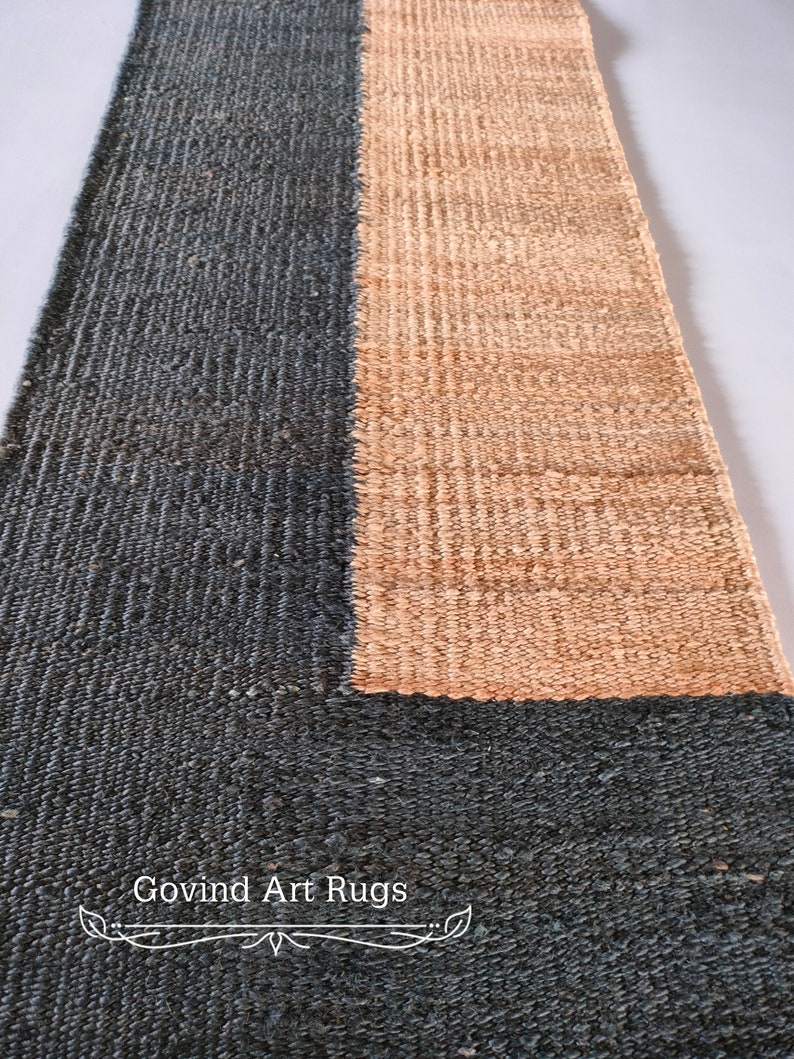 May include: A handwoven rug with a geometric design. The rug is made of natural fibers and has a dark blue and light brown color scheme. The rug is labeled "Govind Art Rugs".