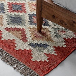 May include: A rectangular area rug with a geometric pattern in red, beige, blue, and brown. The rug has a fringed edge and is partially visible beneath a wooden bed frame.