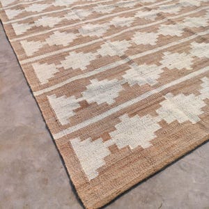May include: A brown and white woven rug with a geometric pattern. The rug is made of natural fibres and has a rustic look.