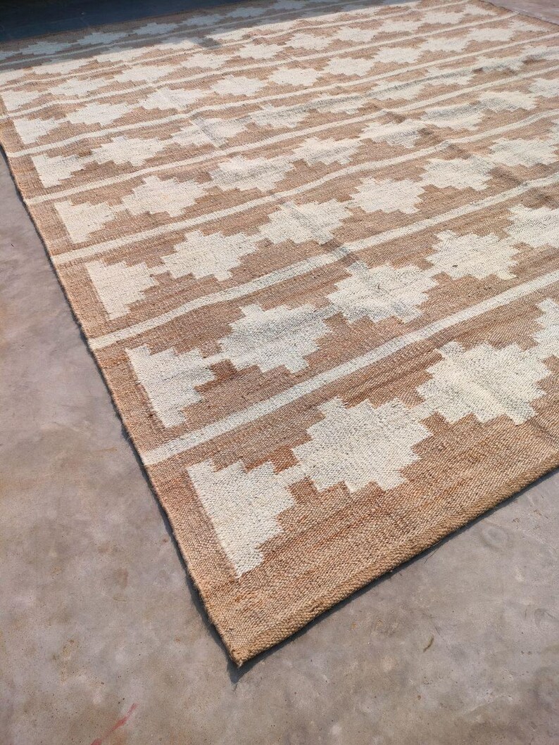 May include: A brown and white woven rug with a geometric pattern. The rug is made of natural fibres and has a rustic look.