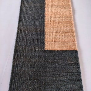 May include: A long, narrow rug with a dark blue and beige color scheme. The rug has a simple geometric design with a rectangular shape in the center. The rug is made of natural fibers and has a textured surface. The text "Govind Art Rugs" is visible at the bottom of the rug.