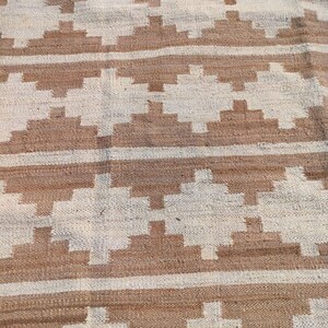 May include: A woven rug with a geometric pattern in shades of brown and white. The rug has a natural, rustic look and feel.