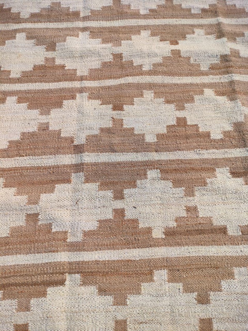 May include: A woven rug with a geometric pattern in shades of brown and white. The rug has a natural, rustic look and feel.