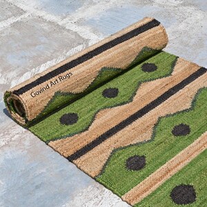 May include: A rolled-up jute rug with a green and tan geometric pattern. The rug features black accents and circular designs. The text "Govind Art Rugs" is visible on the rolled portion of the rug.