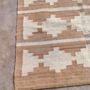 May include: A brown and white woven rug with a geometric pattern. The rug has a fringed border.