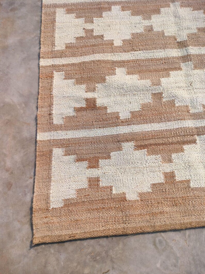 May include: A brown and white woven rug with a geometric pattern. The rug has a fringed border.