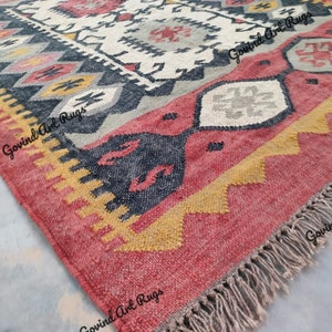 May include: A red, yellow, and gray patterned rug with fringe. The rug has a geometric design with black accents.