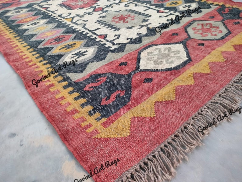 May include: A red, yellow, and gray patterned rug with fringe. The rug has a geometric design with black accents.