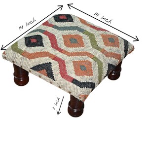 Può includere: Un pouf quadrato con piano fantasia e gambe in legno scuro. Il piano misura 35,5 cm per 35,5 cm, con un disegno geometrico in rosso, arancione, verde e nero. Le gambe sono alte 20,3 cm.