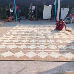 May include: A large, handwoven rug with a geometric pattern in shades of brown and white. The rug is made of natural fibres and has a rustic, earthy feel.