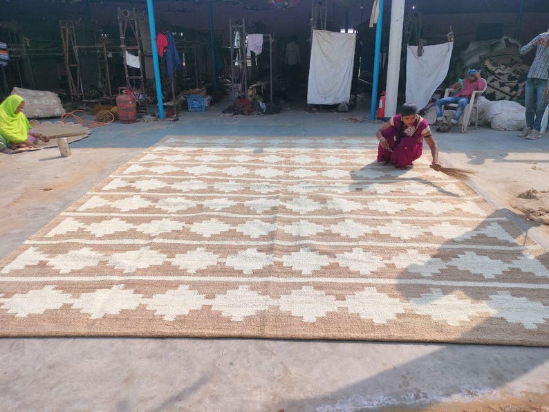 May include: A large, handwoven rug with a geometric pattern in shades of brown and white. The rug is made of natural fibres and has a rustic, earthy feel.