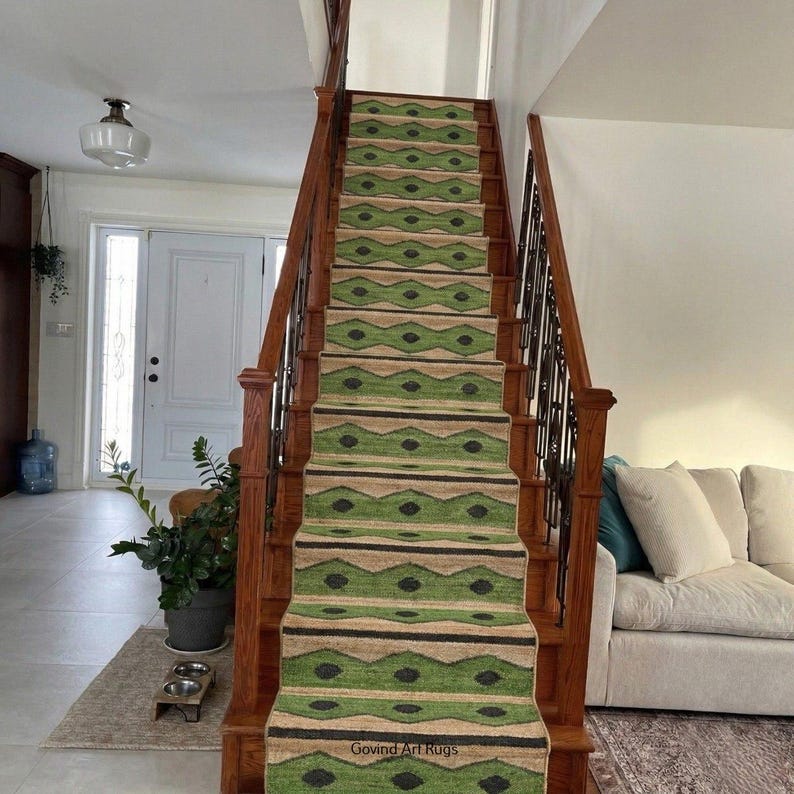 May include: A staircase with a green and tan patterned runner rug. The rug features a repeating geometric design with black accents. The wooden stairs have a dark finish, and the walls are painted white. The text "Govind Art Rugs" is visible.