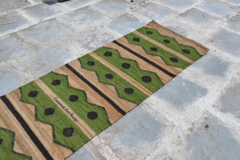 May include: A rectangular runner rug with a geometric pattern. The rug features alternating stripes of green, tan, and black. The green sections have black circular accents. The text "Govind Art Rugs" is visible on the rug.