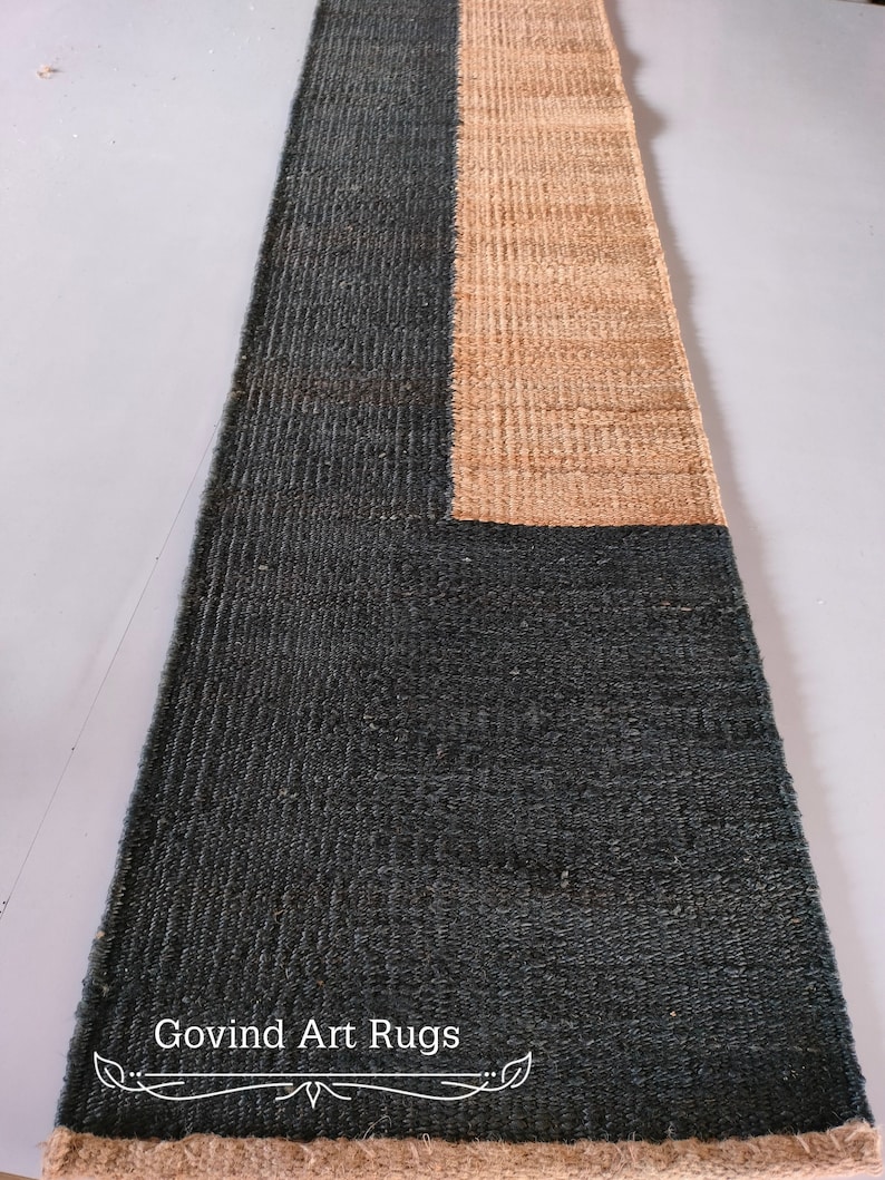 May include: A black and beige rectangular rug with a geometric design. The rug has a fringe border and the text "Govind Art Rugs" is printed on the rug.