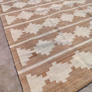 May include: A brown and white woven rug with a geometric pattern. The rug has a natural, earthy feel and would add a touch of texture to any room.