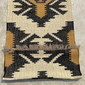 Puede incluir: Una alfombra con estampado geom&eacute;trico en blanco y negro con un borde amarillo mostaza. La alfombra tiene flecos en los bordes.