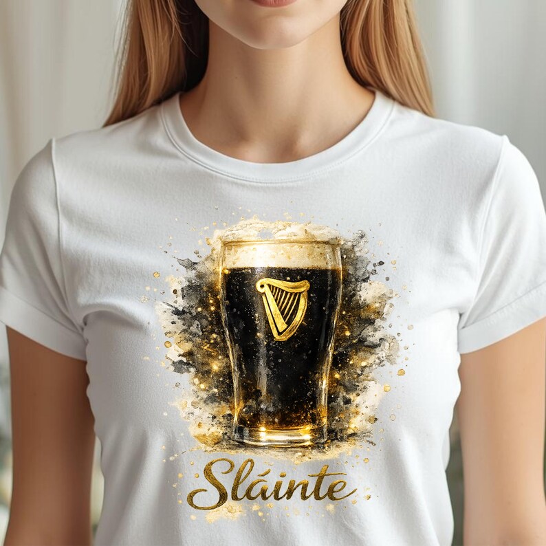 May include: White t-shirt featuring a watercolor-style image of a pint of dark beer with a golden harp logo. The word "Sl&aacute;inte" is written in gold script below the pint. The design has gold and black accents.