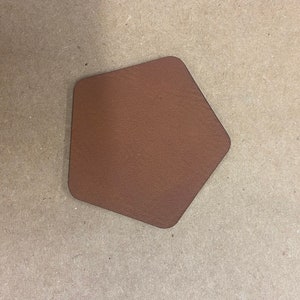 Może przedstawiać: Brązowa skórzana podkładka pod kubek w kształcie sześciokąta.