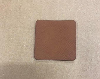 Può includere: Un sottobicchiere in pelle marrone con un bordo leggermente arrotondato.