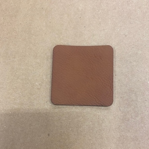 May include: A brown leather coaster with a slightly rounded edge.