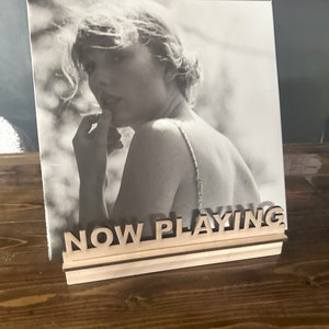 May include: A wooden record stand with the words "NOW PLAYING" in large letters. A black and white photo of a woman is displayed on the stand.